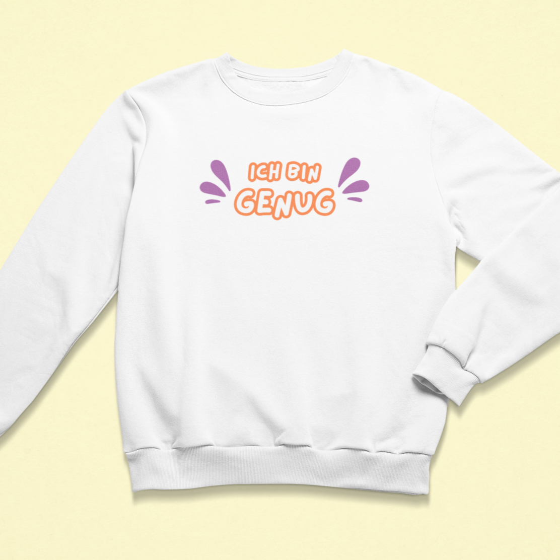 Weißes Kinder-Sweatshirt mit der Aufschrift „Ich bin genug“ in orangefarbener Schrift mit lila Akzenten, auf hellem Hintergrund liegend. Das Design vermittelt Selbstliebe und Achtsamkeit.