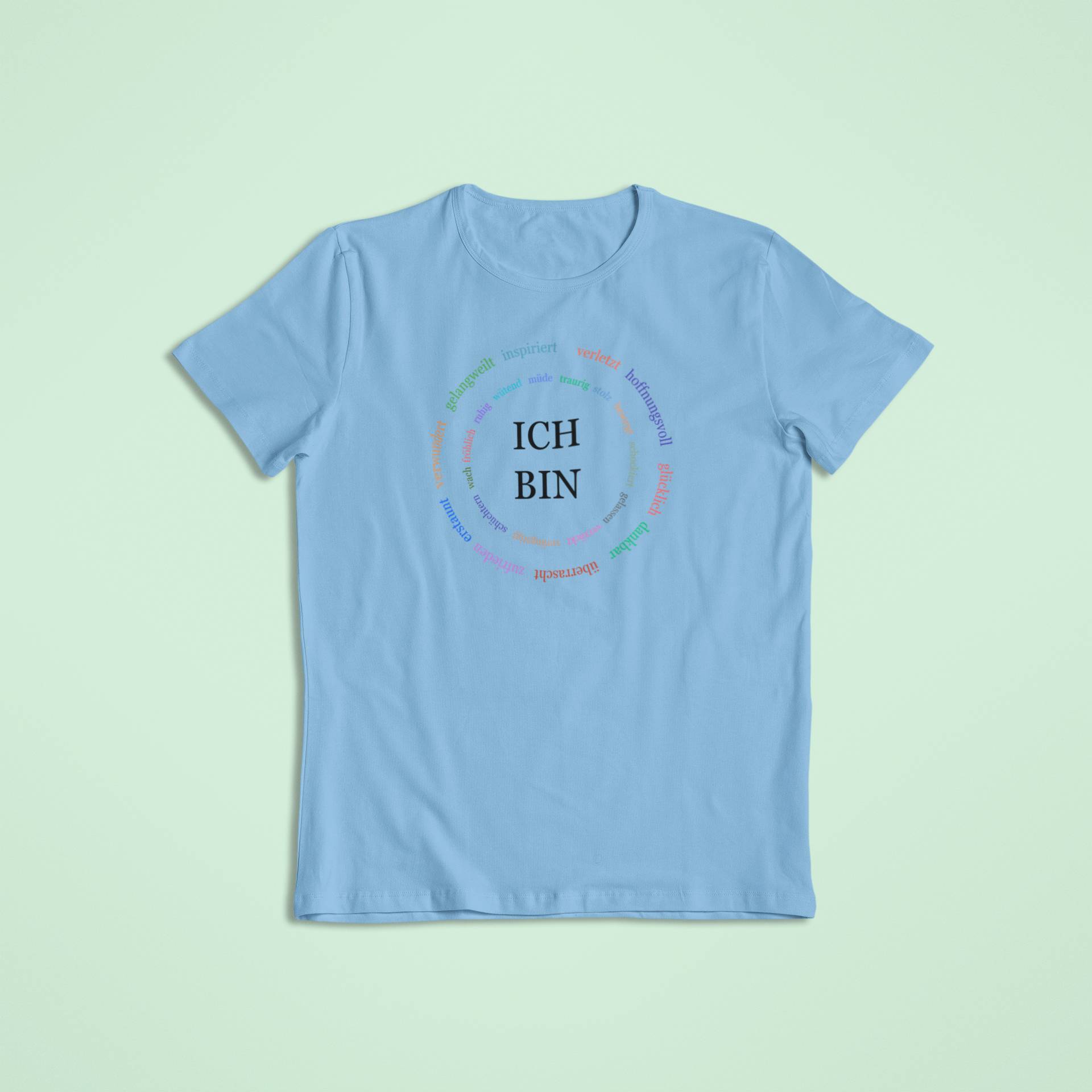 Himmelblaues Kindershirt mit zentralem „ICH BIN“-Schriftzug, umgeben von bunten, kreisförmig angeordneten Affirmationen.
