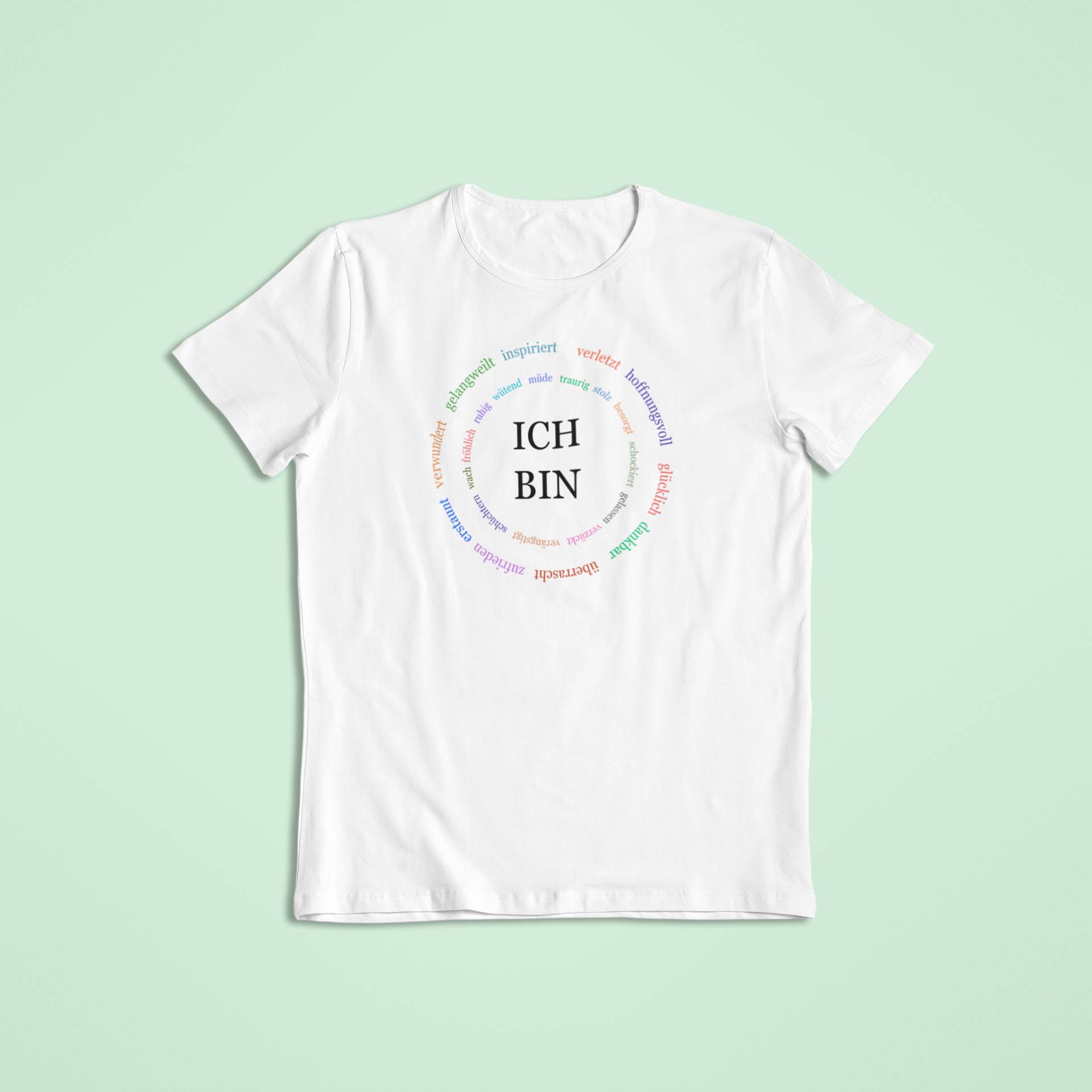 Weißes Kindershirt mit schwarzem „ICH BIN“-Text in der Mitte und einem farbenfrohen Kreis aus positiven Gefühlen und Zuständen.