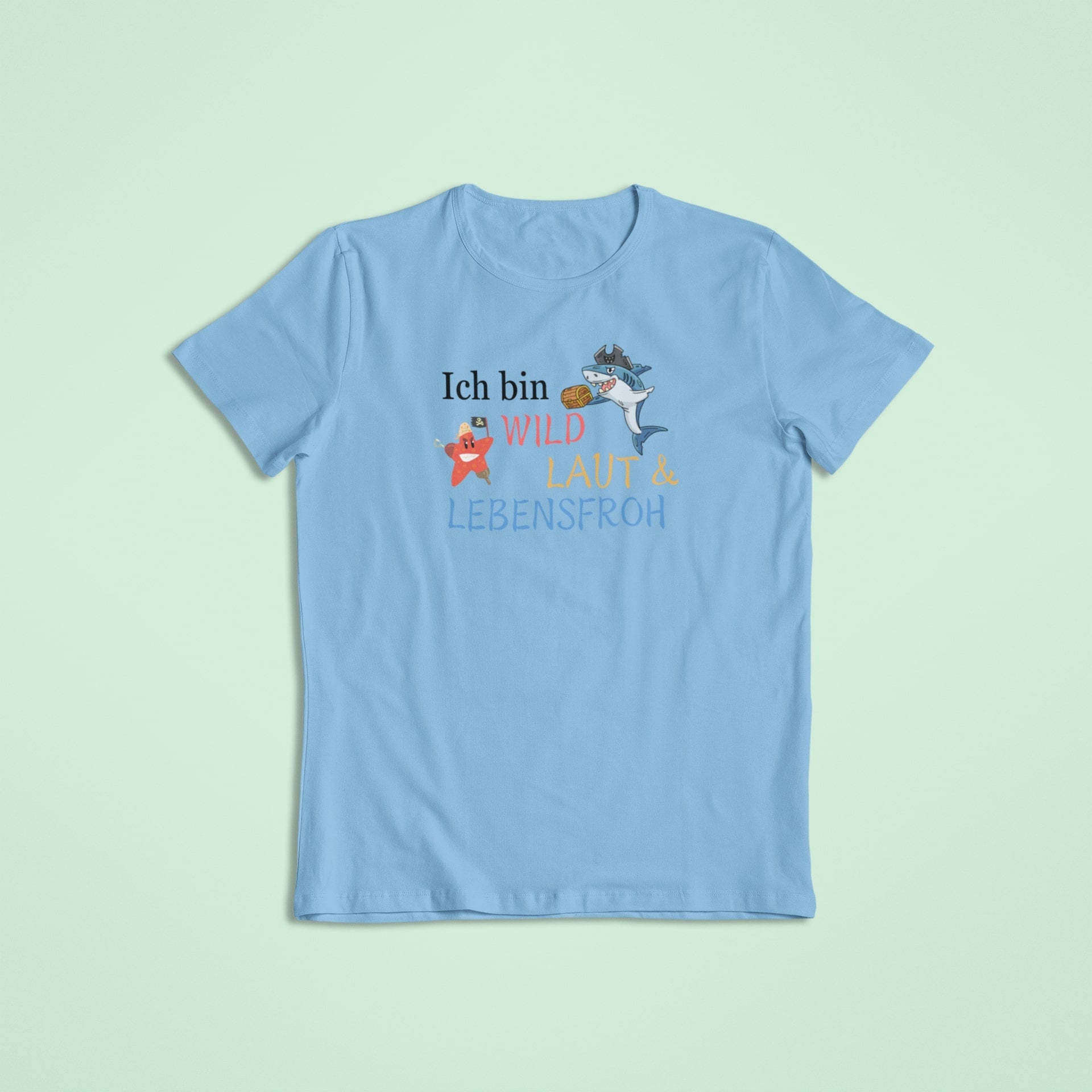 Hellblaues Kindershirt mit lebhafter Aufschrift „Ich bin wild, laut & lebensfroh“, ergänzt durch einen Piraten-Seestern und einen Hai mit Schatzkiste.