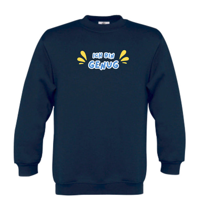 blau Kinder-Sweatshirt mit dem Aufdruck „Ich bin genug“ in farbenfroher Schrift. Das Wort „Ich bin“ ist in orangefarbener Schrift, „Genug“ in dicker, weißer Umrandung mit weißer Füllung. Links und rechts vom Text befinden sich lilafarbene, tropfenförmige Akzente. Das Sweatshirt liegt flach auf einer weißen Oberfläche, dekoriert mit Baumwollzweigen und Eukalyptusblättern.