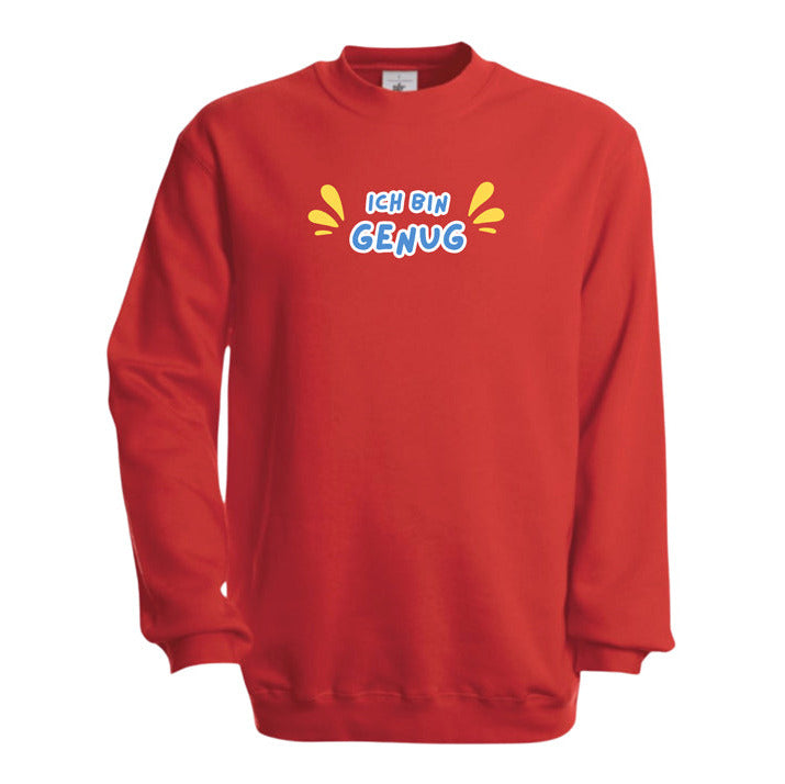 rotes Kinder-Sweatshirt mit dem Aufdruck „Ich bin genug“ in farbenfroher Schrift. Das Wort „Ich bin“ ist in orangefarbener Schrift, „Genug“ in dicker, weißer Umrandung mit weißer Füllung. Links und rechts vom Text befinden sich lilafarbene, tropfenförmige Akzente. Das Sweatshirt liegt flach auf einer weißen Oberfläche, dekoriert mit Baumwollzweigen und Eukalyptusblättern.