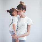Mutter in weißem Statement-T-Shirt mit Aufdruck „Mama. Mit Liebe. Nicht mit Perfektion.“ hält ihr Kind auf dem Arm – liebevolle Szene aus der „Achtsame Mama“-Kollektion vom Sinachtsam-Shop