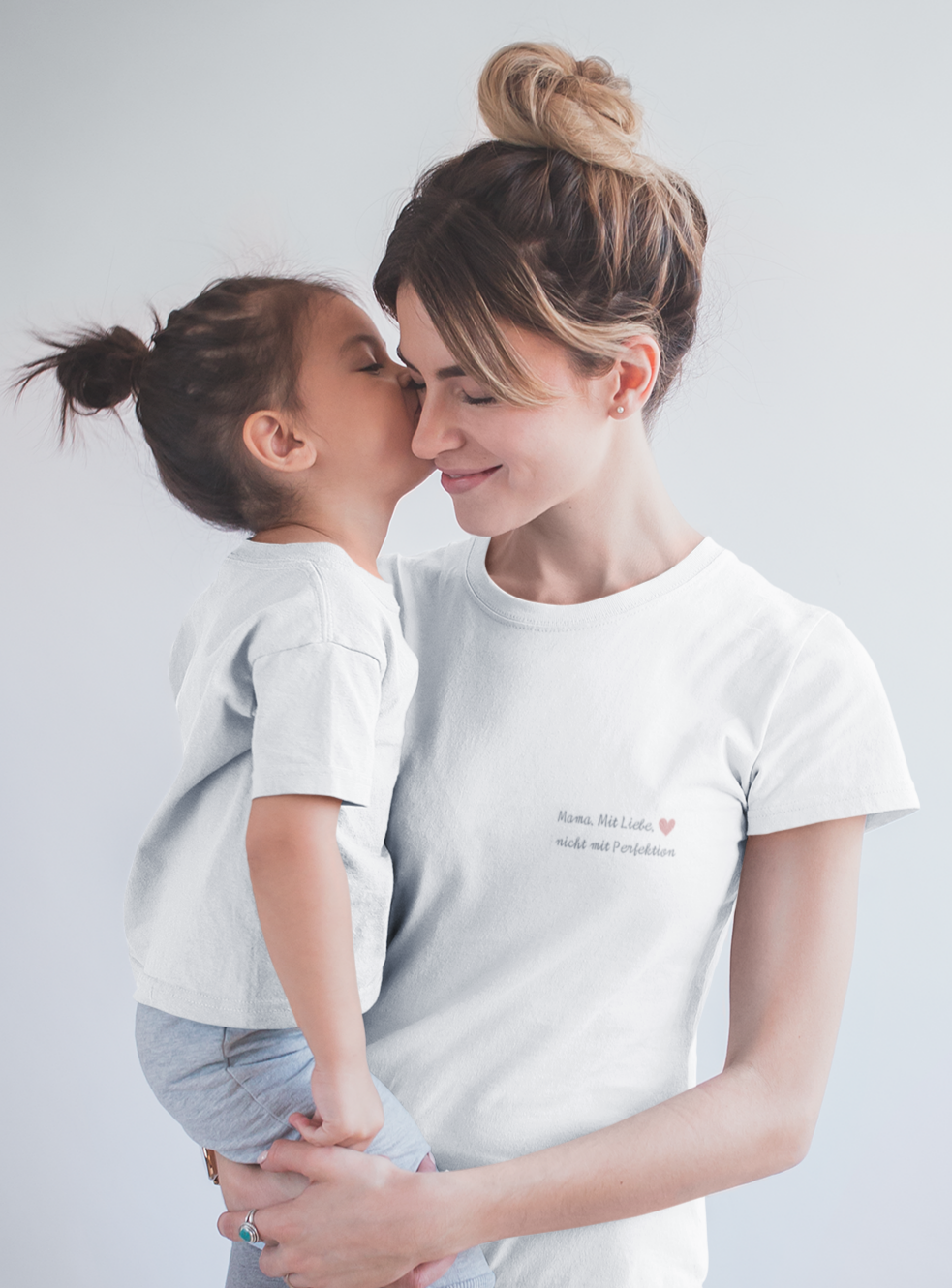Mutter in weißem Statement-T-Shirt mit Aufdruck „Mama. Mit Liebe. Nicht mit Perfektion.“ hält ihr Kind auf dem Arm – liebevolle Szene aus der „Achtsame Mama“-Kollektion vom Sinachtsam-Shop