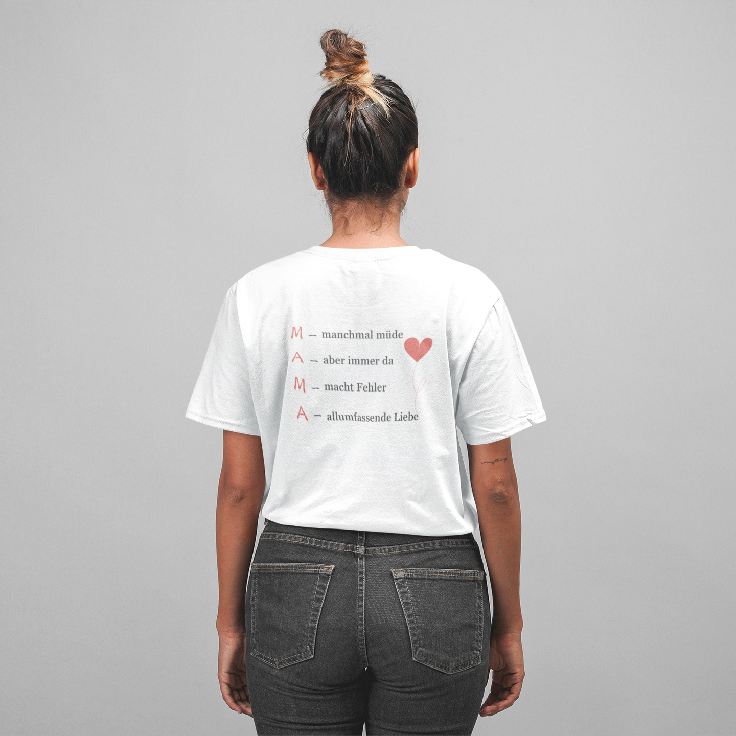 Frau trägt weißes T-Shirt mit Rückseitendruck „M – manchmal müde, A – aber immer da, M – macht Fehler, A – allumfassende Liebe“ und rosa Herzballon – emotionales Mama-Shirt vom Sinachtsam-Shop.