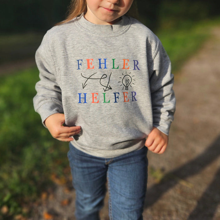 grauer pullover mit schwarzen icons und pfeilen, eine bunte schrift ziert Fehler Helfer