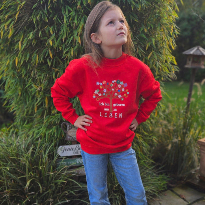 roter pullover mit einem bunten baum drauf und der weißen schrift ich bin geboren um zu leben