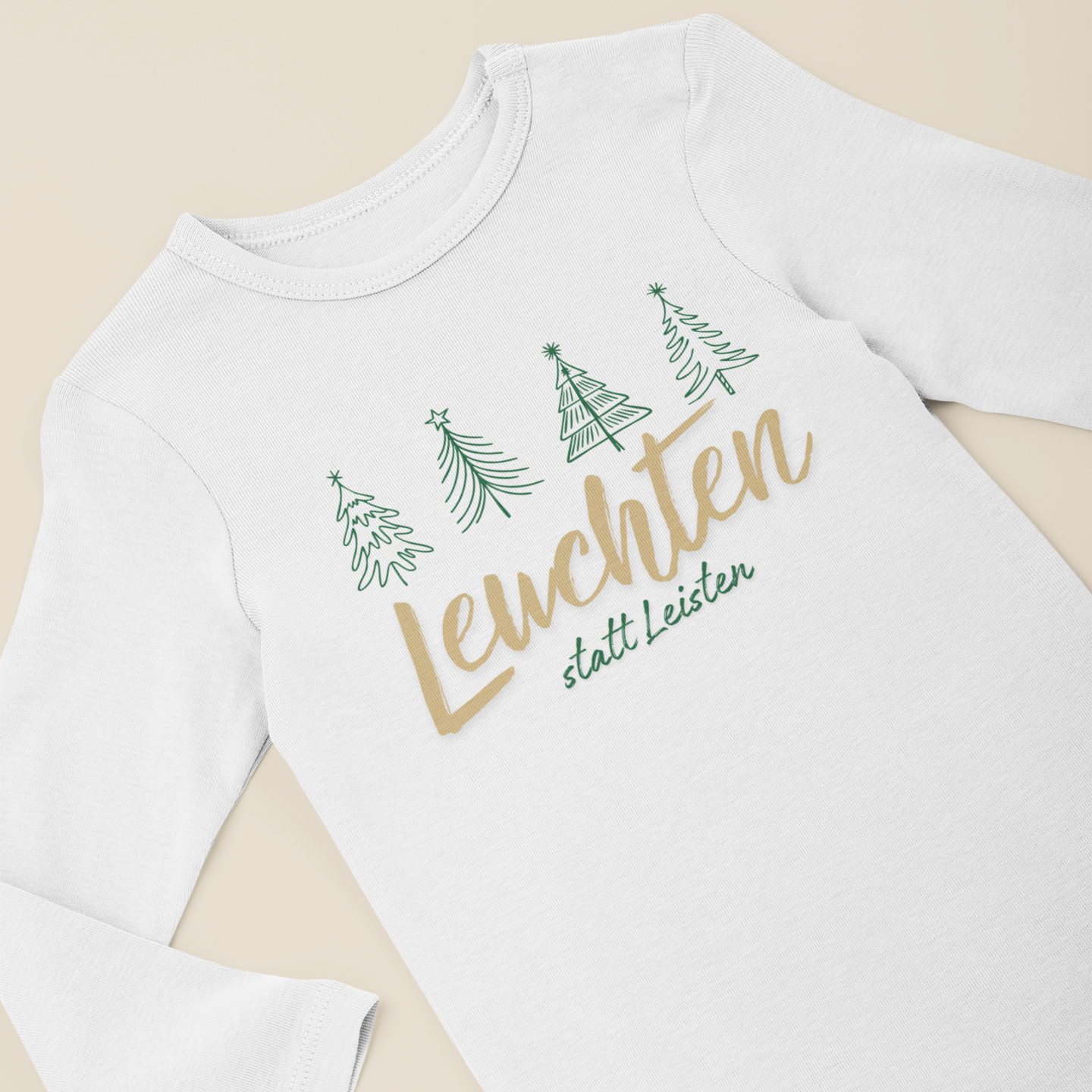 Weißer Baby-Langarmbody mit grünen Tannenbäumen und goldenem Schriftzug „Leuchten statt Leisten“, flach auf hellem Hintergrund präsentiert.