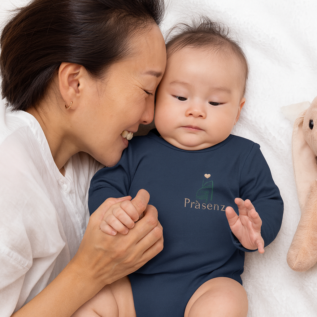 Mama kuschelt mit ihrem Baby, das einen navyfarbenen Body mit kleinem Frontprint „Präsenz“ und Geschenk-Icon trägt.