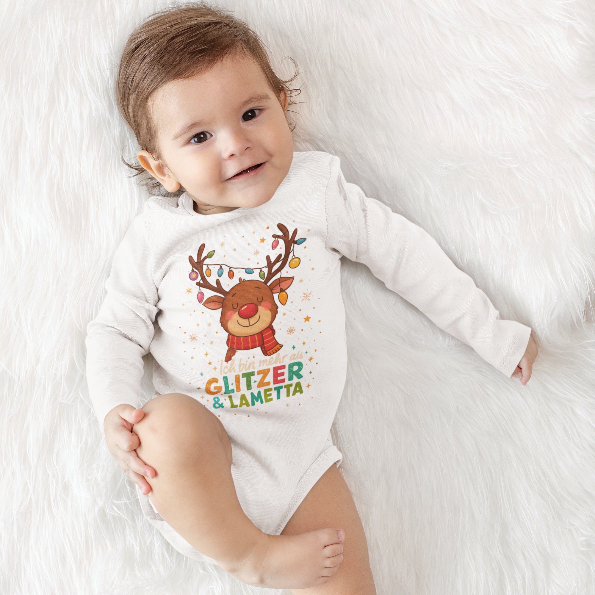 Lächelndes Baby in weißem Weihnachts-Body mit süßem Rentierprint und dem Schriftzug „Ich bin mehr als Glitzer und Lametta“, auf weichem Felluntergrund liegend.