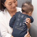 Mama hält ihr Baby auf dem Arm, das einen navyfarbenen Weihnachts-Body mit Rückprint „Ich schenke Präsenz – nicht Präsente“ und weihnachtlichen Icons trägt.