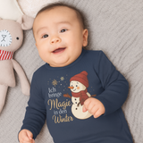 Baby trägt einen navyfarbenen Weihnachts-Langarmbody mit Schneemann und dem Spruch „Ich bringe Magie in den Winter“ – festliche, liebevolle Szene im Winter-Look.