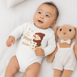 Baby trägt einen weißen Weihnachts-Langarmbody mit Schneemann und dem Spruch „Ich bringe Magie in den Winter“ – gemütliche Winter-Szene mit Stofftier.