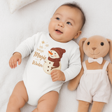 Baby trägt einen weißen Weihnachts-Langarmbody mit Schneemann und dem Spruch „Ich bringe Magie in den Winter“ – gemütliche Winter-Szene mit Stofftier.