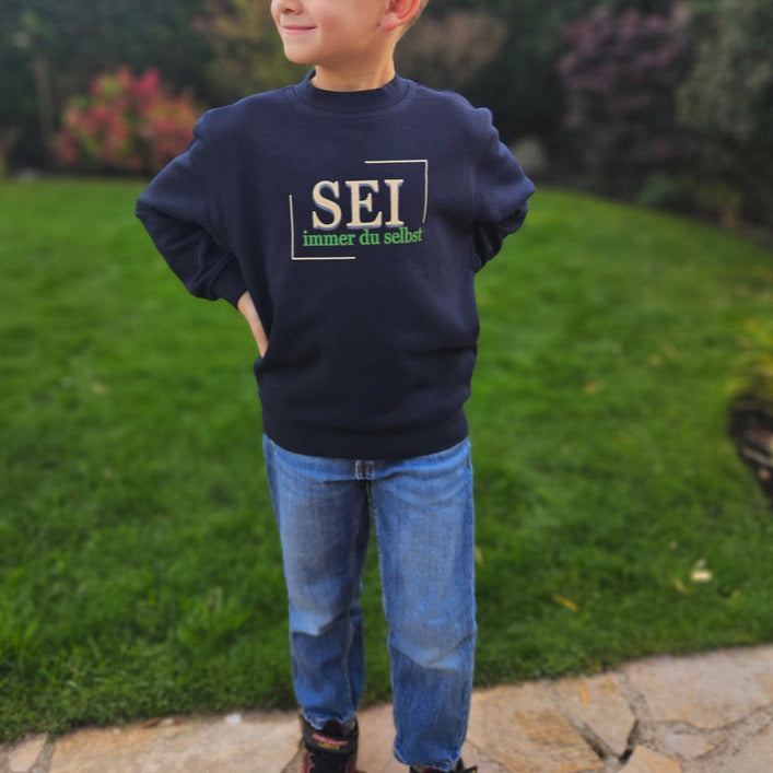 dunkelblauer statement pullover mit der aufschrift in beige und grün: sei immer du selbst