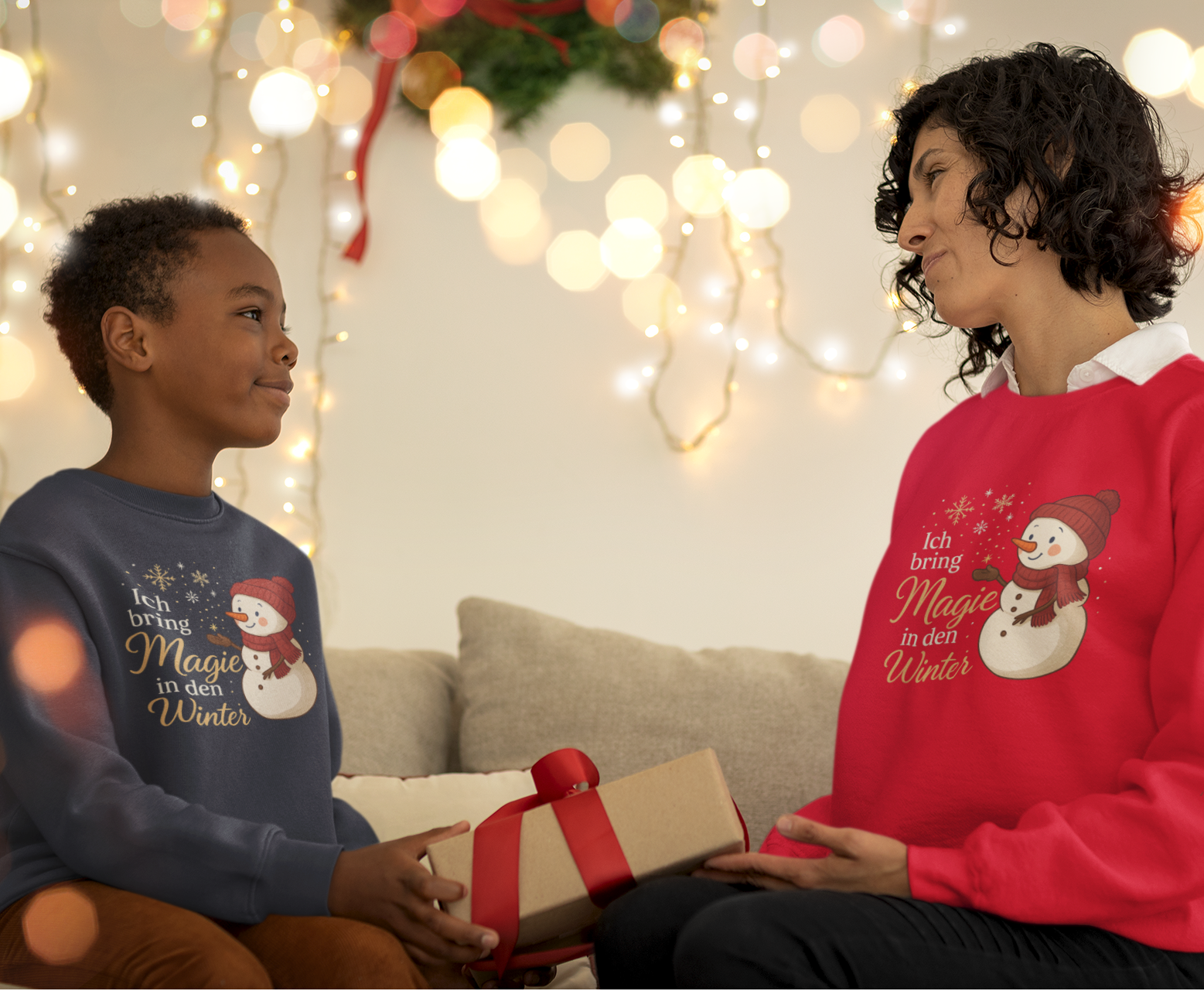 Mutter und Kind tragen weiße Weihnachtssweater mit Schneemann und Affirmation „Ich bring Magie in den Winter“.