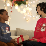 Mutter und Kind tragen weiße Weihnachtssweater mit Schneemann und Affirmation „Ich bring Magie in den Winter“.