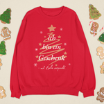Rotes Weihnachtssweatshirt mit goldener Tannenbaum-Grafik und dem Schriftzug „Ich bin ein Geschenk – mit Liebe verpackt“, umgeben von Lebkuchenfiguren und festlicher Deko.