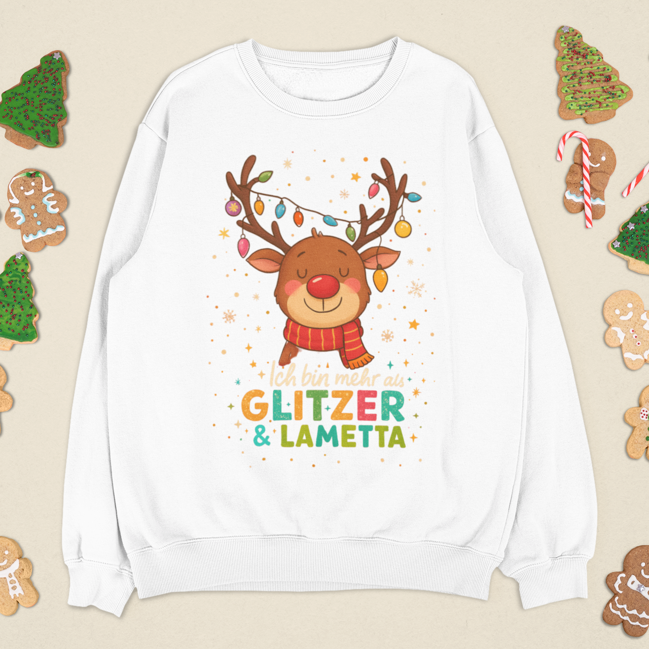 Weißes Sweatshirt mit Rentier, Lichterkette und der Botschaft ‚Ich bin mehr als Glitzer & Lametta‘, dekoriert mit Weihnachtskeksen.