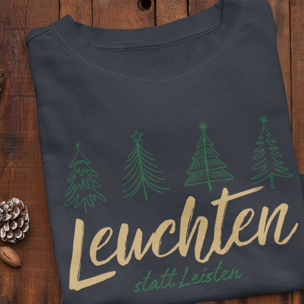 Dunkelblaues Weihnachtssweatshirt mit grünen Tannenbäumen und goldener Aufschrift „Leuchten statt Leisten“ – achtsame Weihnachtsmode von Sinachtsam.