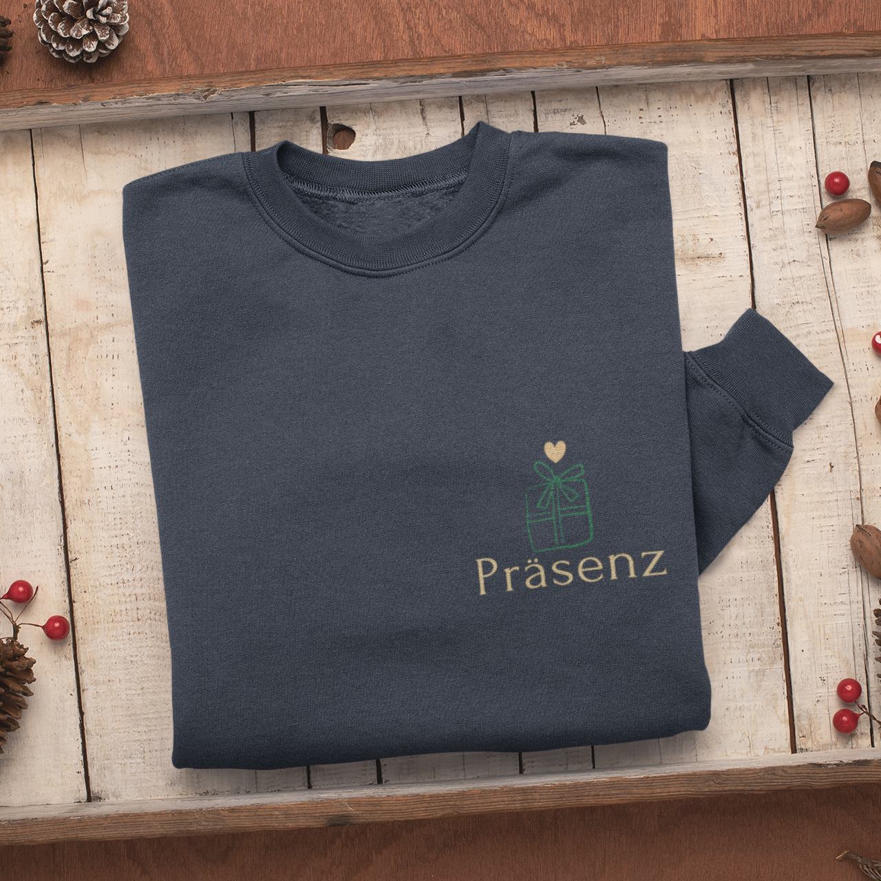 Gefaltetes dunkelblaues Sweatshirt auf rustikalem Holztablett, mit kleinem Frontprint Präsenz und Geschenk-Icon.