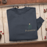 Gefaltetes dunkelblaues Sweatshirt auf rustikalem Holztablett, mit kleinem Frontprint Präsenz und Geschenk-Icon.