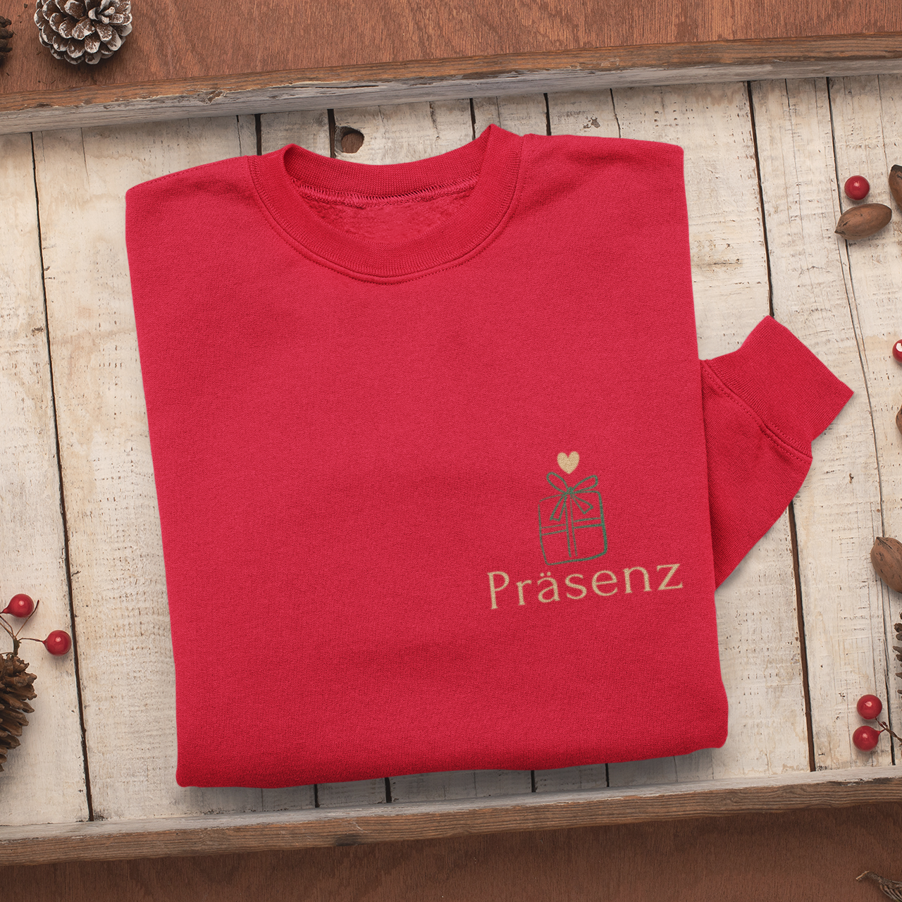 Gefaltetes rotes Sweatshirt auf Holztablett mit kleinem Frontprint Präsenz und einem grünen Geschenk-Icon mit Herz